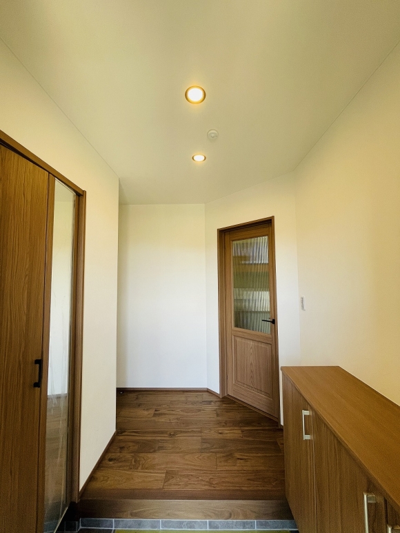 玄関を入ると、白ベースのクロスに暖かみのある色味を使用した床材、建具で落ち着いた空間です。