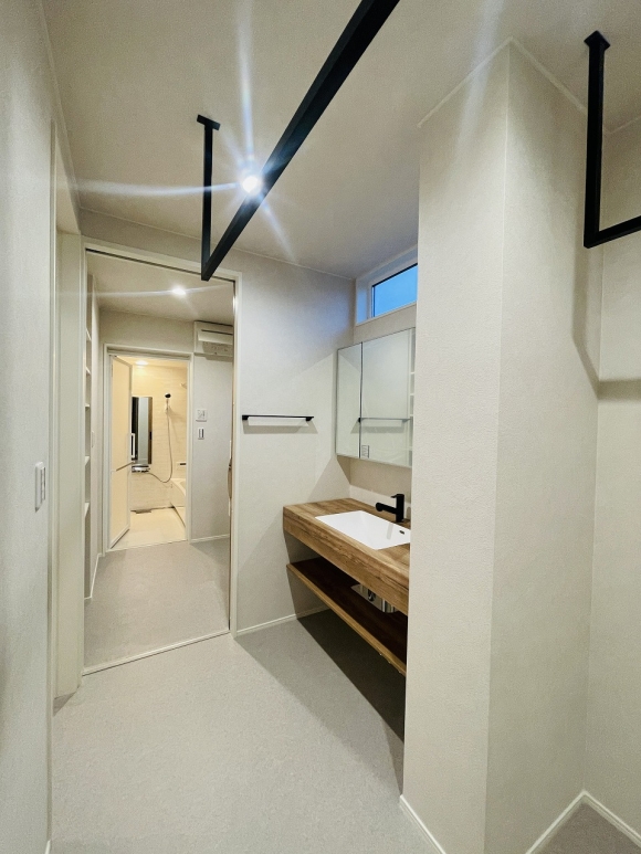 造作洗面台と黒のランドリーパイプが映えるスペースは脱衣室、浴室へ一直線のスムーズな動線です。